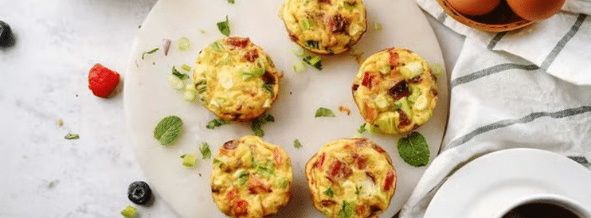 Muffins aux œufs healthy aux légumes et herbes fraîches disposés sur un plateau en marbre blanc avec des baies à côté.
