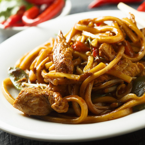 Gros plan sur nouilles sautées au poulet avec sauce à l’ail caramélisé et légumes croquants.