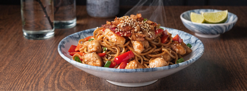 Bol de nouilles au poulet à l’ail caramélisé avec poivrons, graines de sésame et sauce brillante.