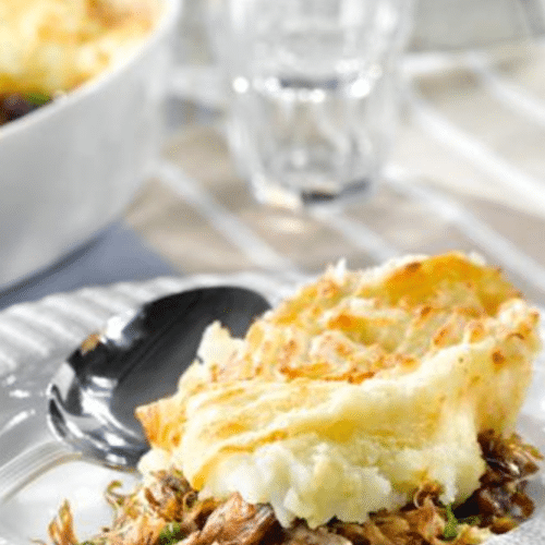 Part de parmentier de confit de canard servie dans une assiette avec purée gratinée.
